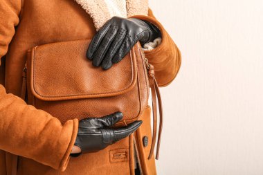 Siyah deri eldivenli, parlak arka planda şık çantalı bir kadın, yakın plan.