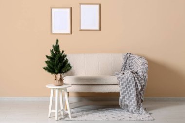 Bej duvarın yanındaki kanepede küçük bir Noel ağacı.