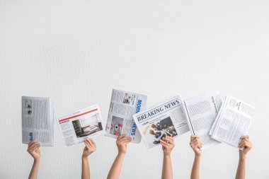 Female hands with different newspapers against light background clipart