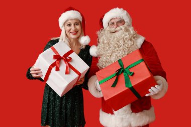 Noel Baba ve kırmızı arka planda hediye kutuları olan güzel olgun bir kadın.