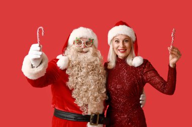 Noel Baba ve kırmızı arka planda baston şekerlerle Noel şapkalı güzel olgun bir kadın.