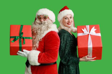 Noel Baba ve yeşil arka planda hediye kutularıyla Noel şapkalı güzel olgun kadın.