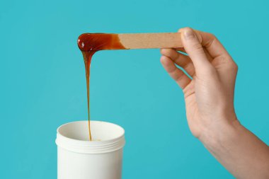 Turkuaz arka planda tüy aldırmak için bir kavanoz şekerleme macunu ile kadın eli.