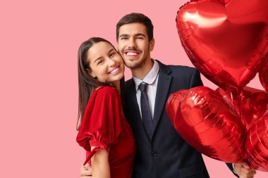 Pembe arka planda kalp şeklinde balonları olan genç ve güzel bir çift. Sevgililer Günü kutlaması