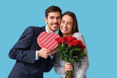 Kırmızı gül buketi ve mavi arka planda hediye kutusu olan güzel bir çift. Sevgililer Günü kutlaması