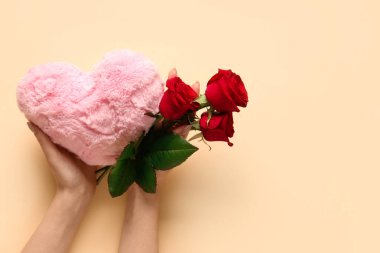 Güzel kırmızı gülleri ve sarı arka planda oyuncak kalbi olan kadın elleri. Sevgililer Günü kutlaması