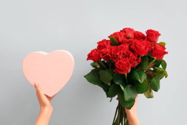 Kırmızı gül buketi ve mavi arka planda hediye kutusu olan kadın elleri. Sevgililer Günü kutlaması
