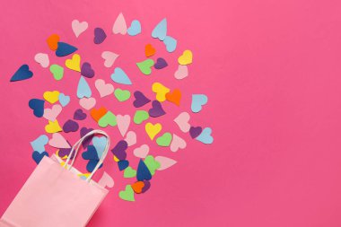 Pembe arka planda alışveriş torbası olan farklı kağıt kalpler. Sevgililer Günü kutlaması