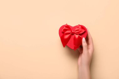 Bej arka planda hediye kutusu olan bir kadın eli. Sevgililer Günü kutlaması