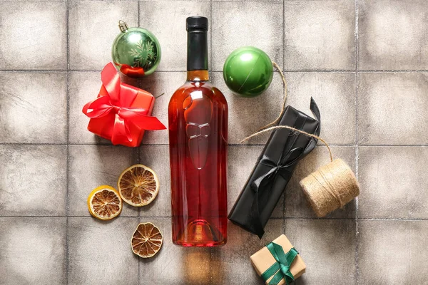 Bottle of wine with Christmas balls, gift boxes and dried orange on grey tile background