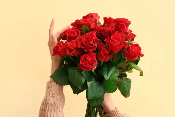 Female hands with bouquet of beautiful red roses on yellow background. Valentine\'s day celebration