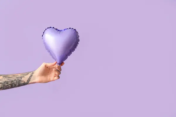 Man with air balloon in shape of heart on lilac background. Valentine\'s Day celebration