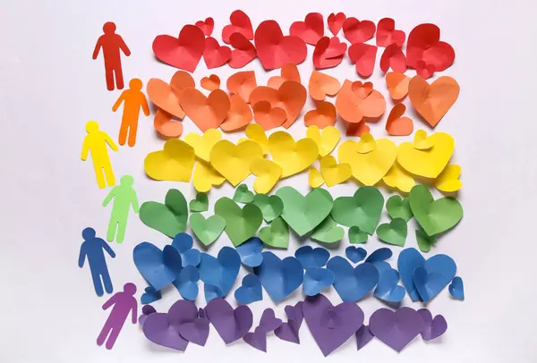 Paper hearts and human figures in colors of LGBT flag on grey background. Valentine\'s Day celebration