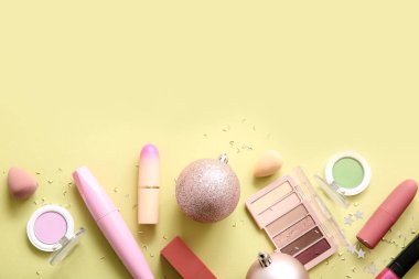 Dekoratif kozmetik ürünleri ve açık sarı arka planda pembe Noel topları içeren kompozisyon