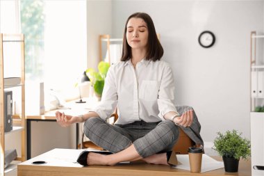 Genç iş kadını ofiste meditasyon yapıyor.
