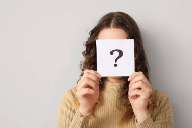 Gri arka planda soru işareti olan kağıt kağıtları tutan genç bir kadın.
