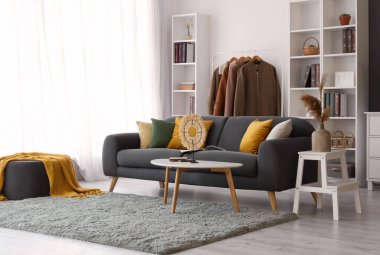 Oturma odasının içinde siyah kanepe ve elbise askısı var.