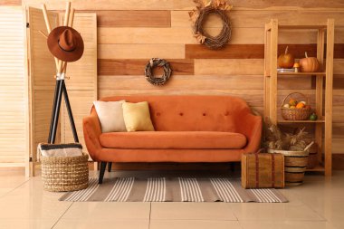 Oturma odasının içinde kahverengi kanepe, raf, çelenk ve balkabakları raflarda.