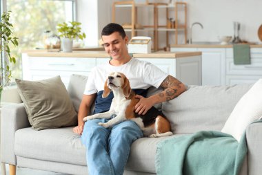Evdeki kanepede oturan sevimli Beagle köpeği olan genç adam.