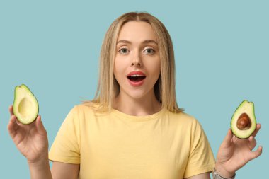 Mavi arka planda avokadosu olan şaşırmış genç bir kadın.