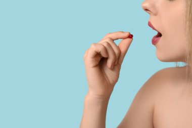 Genç bir kadın mavi arka planda A vitamini hapı alıyor, yakın plan.