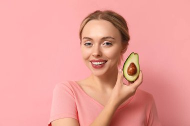 Pembe arka planda avokadosu olan genç bir kadın, yakın plan.