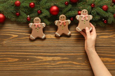 Noel tatlısı zencefilli kurabiyeler ve tahta arka planda köknar dallarıyla kadın eli.