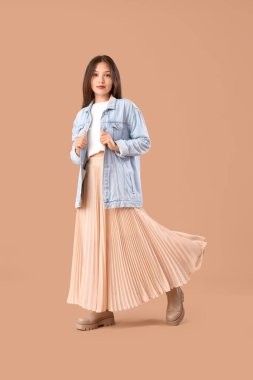 Kahverengi arka planda şık giyinmiş Asyalı genç bir kadın.