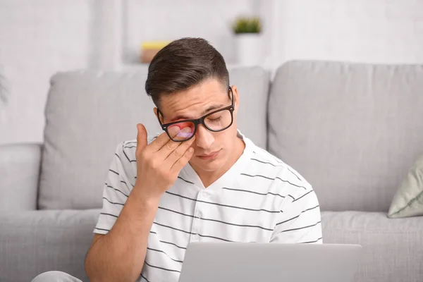 Tired young man rubbing eyes while working on laptop at home
