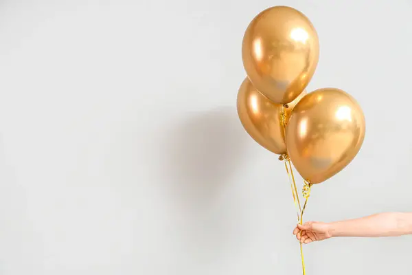 Female hand with golden balloons for birthday celebration on light background