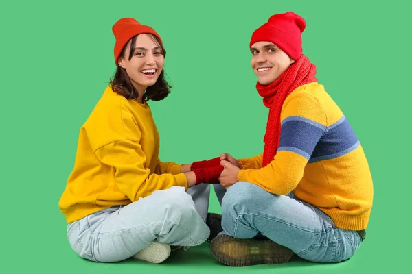 stock image Happy young couple in warm clothes sitting on green background