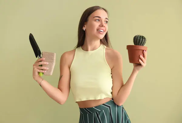 Schöne Junge Frau Mit Kaktus Und Gartengeräten Auf Grünem Hintergrund — Stockfoto