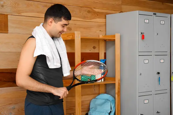 Sporty young man with tennis racket in locker room