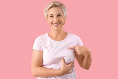 Güzel olgun bir kadın pembe arka planda göğüslerini kontrol ediyor. Kanser farkındalığı kavramı