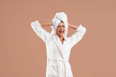 Kahverengi arka planda duş aldıktan sonra bornozlu genç Afro-Amerikalı kadın