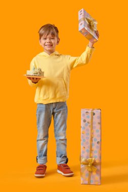 Doğum günü pastası ve sarı arka planda hediyeleri olan sevimli küçük bir çocuk.