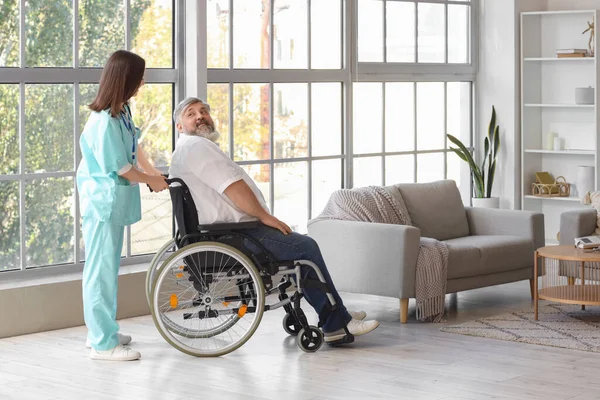 Mature man in wheelchair with nurse at home