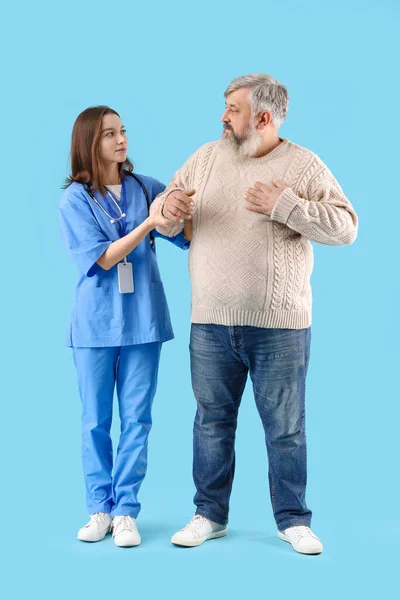 Mature man with nurse holding hands on blue background