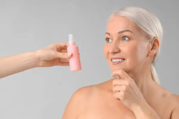 stock image Beautiful mature woman and hand with bottle of skincare product on light background, closeup