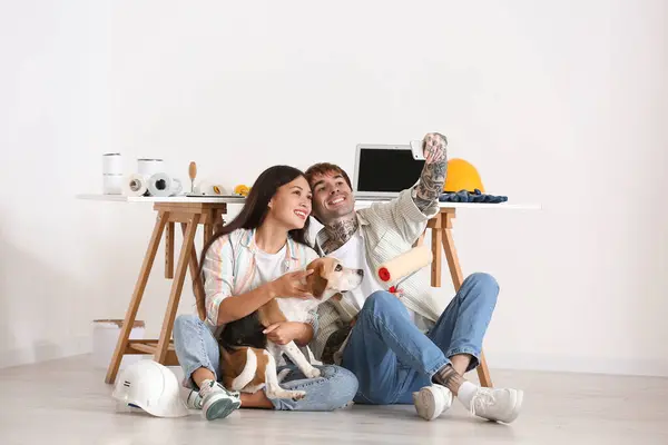 Young couple with Beagle dog and paint roller taking selfie during repair in their new house