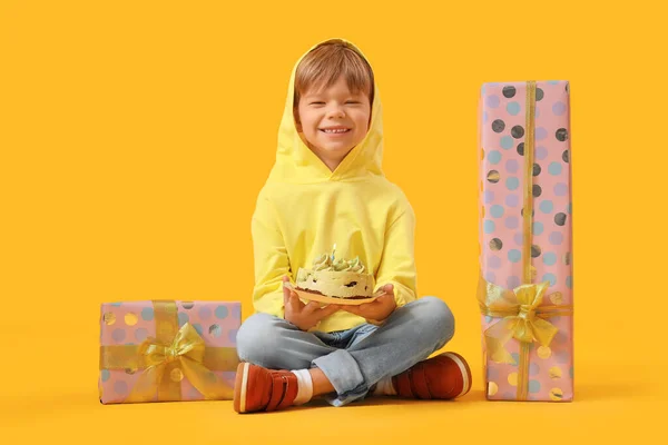 Cute little boy with Birthday cake and gifts sitting on yellow background
