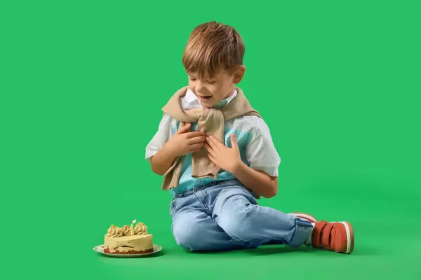 Cute little boy with Birthday cake sitting on green background