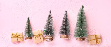 Hediyeli Noel ağaçları ve pembe arka planda kar