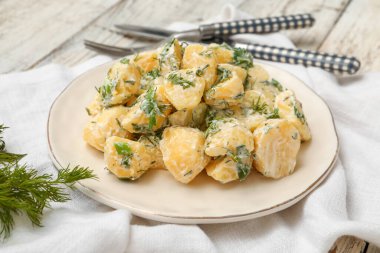 Hafif ahşap arka planda yeşillikleri olan lezzetli patates salatası tabağı.