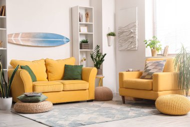 Sörf tahtası, sarı kanepesi ve koltuğu olan bir oturma odası.