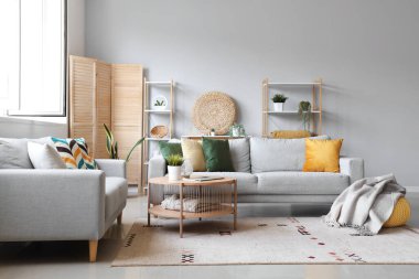 Işıl ışıl oturma odasının iç tarafında yumuşak battaniyeli rahat gri koltuklar ve puf.