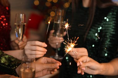 Evde Noel 'i kutlamak için maytap ve bir bardak şampanya taşıyan genç ve güzel kadınlar.