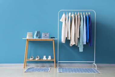 Mavi duvarın yanında şık kıyafetler, ayakkabılar ve aksesuarlarla dizilin.