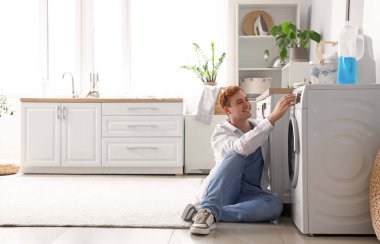 Genç adam evde çamaşır makinesini açıyor.