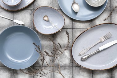 Seramik tabaklar, çatal bıçak takımı ve gri fayanslı arka planda kurutulmuş çiçek dekoru ile güzel bir masa.